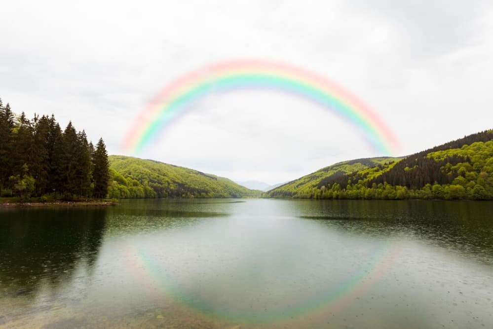 Arco iris completo sobre un tranquilo lago rodeado de colinas boscosas