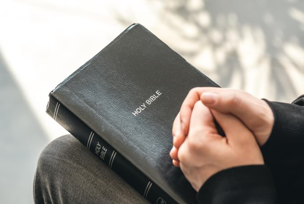Manos entrelazadas sobre una Biblia negra cerrada